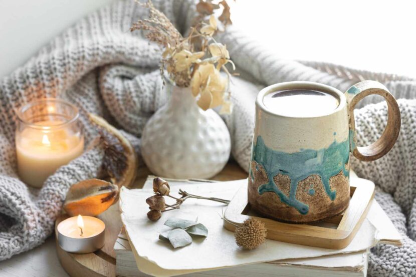 A cozy winter scene with a steaming mug, cinnamon sticks, gingerbread cookies, and a candle, perfect for a 30-Day Winter Self-Care Challenge, set against a snowy backdrop