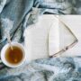 Aesthetic cozy home sanctuary with a soft beige blanket, an open book, and a steaming cup of herbal tea in warm morning sunlight.