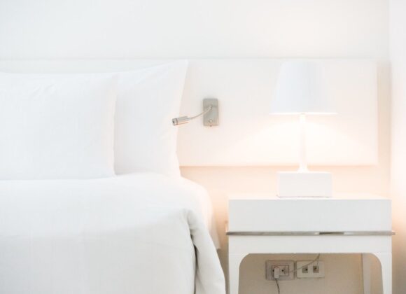 Aesthetic luxury white hotel bed with fluffy pillows, a double-stuffed duvet, and a chunky knit throw blanket in a bright bedroom.