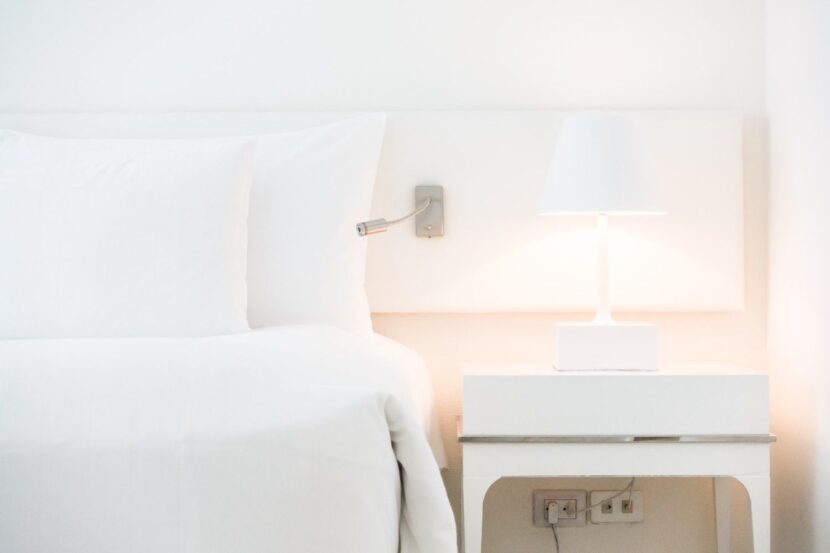 Aesthetic luxury white hotel bed with fluffy pillows, a double-stuffed duvet, and a chunky knit throw blanket in a bright bedroom.