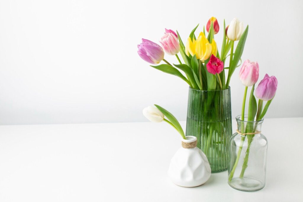 Clear glass vase filled with fresh white tulips sitting on a clean wooden table in a bright, sun-filled room.