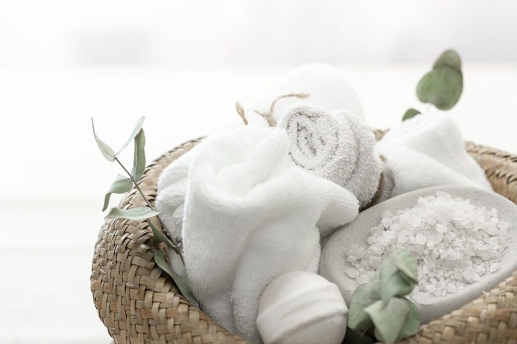 Luxury bathroom aesthetic featuring dried eucalyptus hanging in a shower, clean white rolled towels, and organic soap bars.