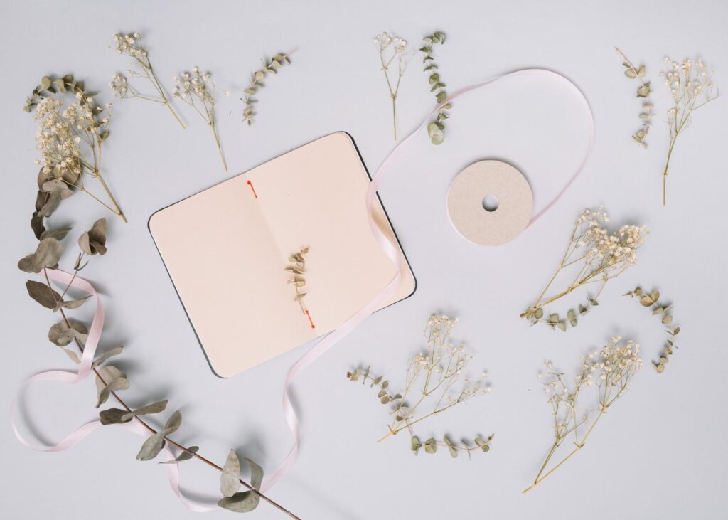 A linen-covered journal laying open on a bed with a small sprig of dried flowers, representing spring mental self-care and goal setting.