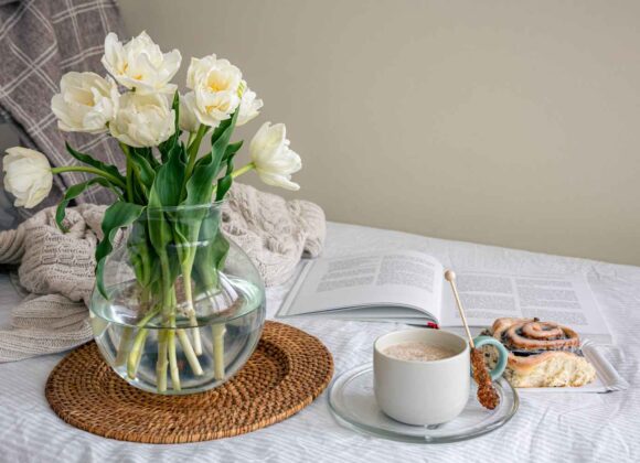 A bright and airy aesthetic morning scene with sunlight streaming through an open window onto white linen sheets and a small vase of spring flowers.