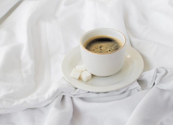 A bright, high-quality photo of a steaming coffee mug next to an open planner on a white desk with soft morning sunlight, perfect for Tuesday morning inspiration.