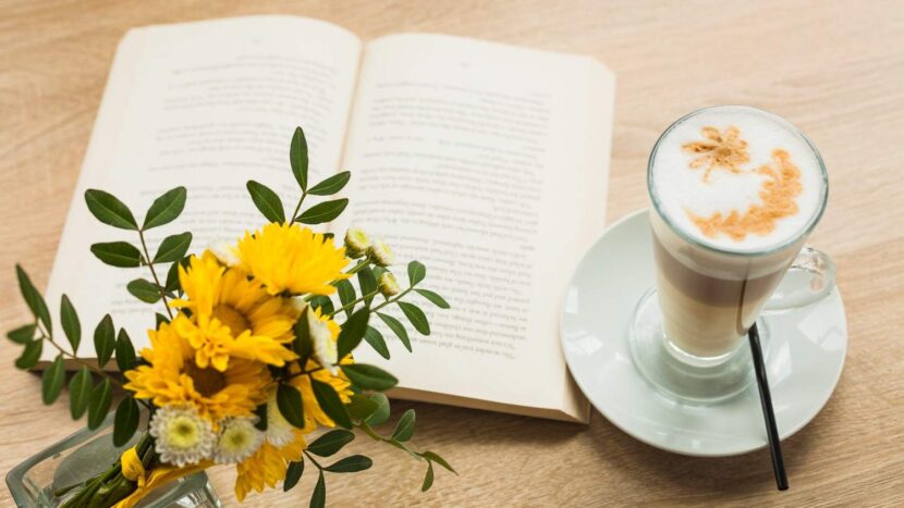 Aesthetic sunny summer desk setup featuring an open journal, a cup of coffee, and a bouquet of yellow flowers in the June sunlight.