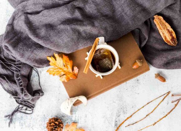 Cozy fall morning routine flat lay with warm coffee mug, knit blanket, and autumn leaves
