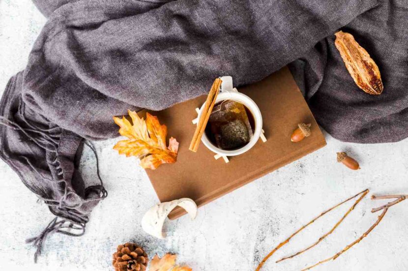 Cozy fall morning routine flat lay with warm coffee mug, knit blanket, and autumn leaves