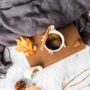 Cozy fall morning routine flat lay with warm coffee mug, knit blanket, and autumn leaves
