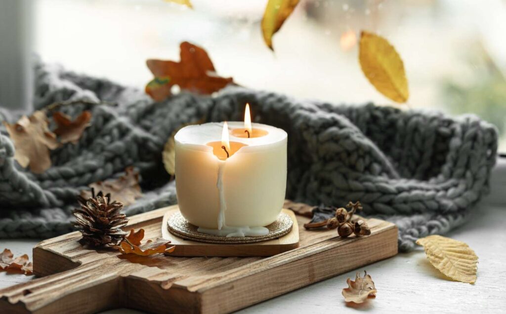 Lit candle on a wooden tray next to a cozy knit sweater during a fall morning routine