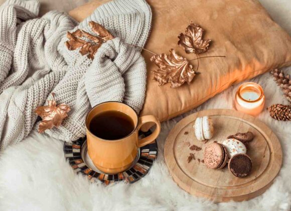 Cozy fall self care flat lay with a candle, warm blanket, tea, and autumn leaves on a wooden table