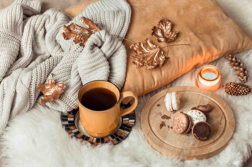 Cozy fall self care flat lay with a candle, warm blanket, tea, and autumn leaves on a wooden table