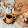 Cozy fall self care flat lay with a candle, warm blanket, tea, and autumn leaves on a wooden table